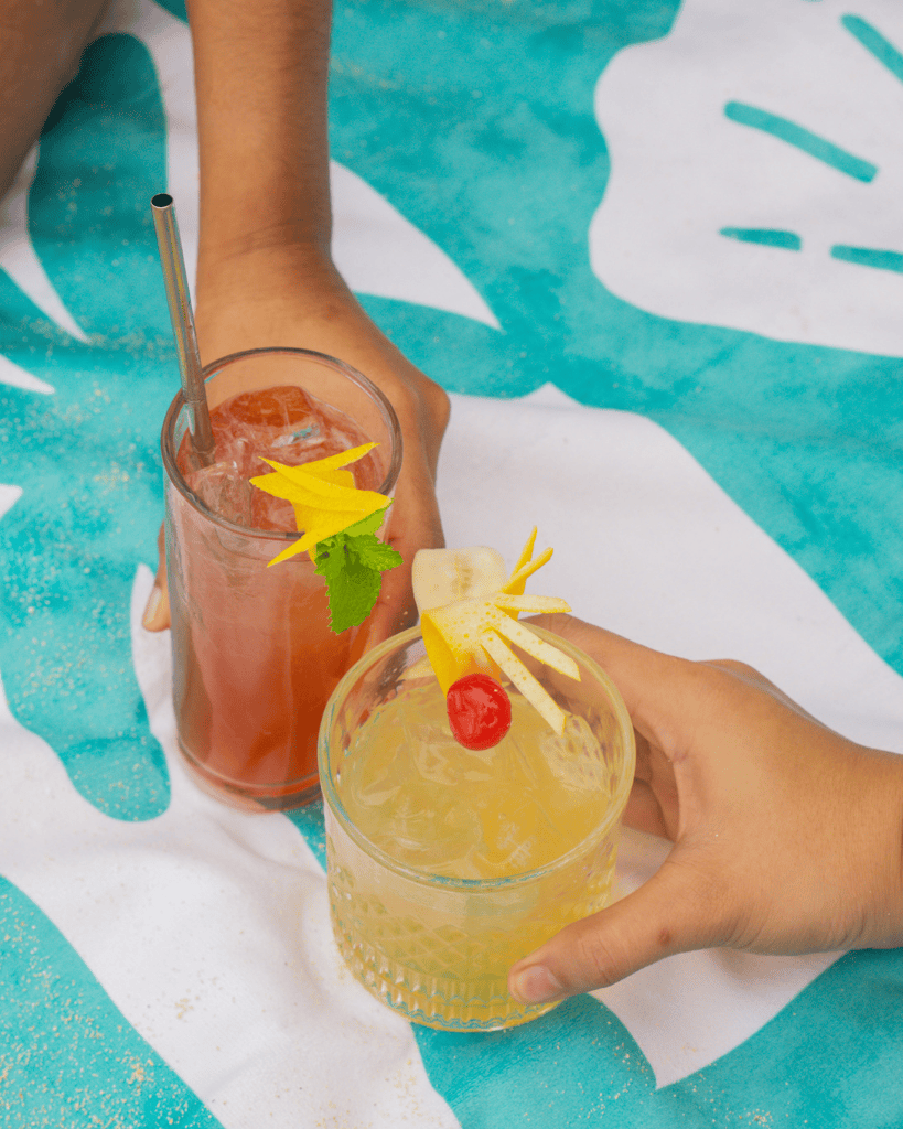 Two cocktails being held on a teal towel