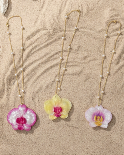 Three orchid necklaces with pink, yellow, and white flowers on a sandy background.