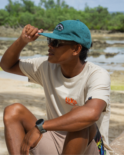 Person wearing a teal cap and sunglasses, sitting outdoors with a natural background