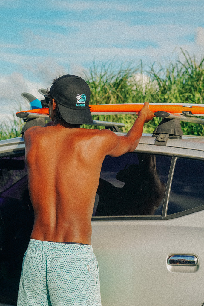 A person wearing a black 'Swell Dad Cap' from the On Cloud 9 Collection, standing next to a vehicle.